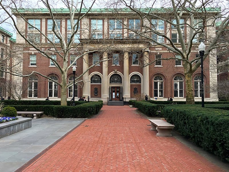 A brick library stands at the end of a red brick path bordered on one side by a perfectly square green hedge