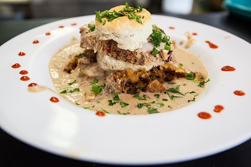Biscuits and gravy on a large white plate dotted with hot sauce.