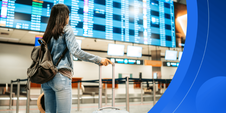 A female international student wearing casual clothes and holding luggage stands in front of a large screen with flight information at an airport.