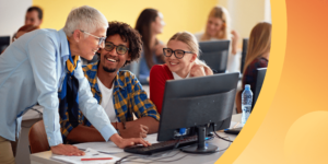 An instructor speaks with two international students in a sunny classroom, surrounded by other students.