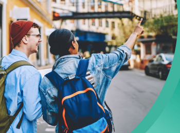 Two students walk along an urban street, wearing backpacks and fall clothing
